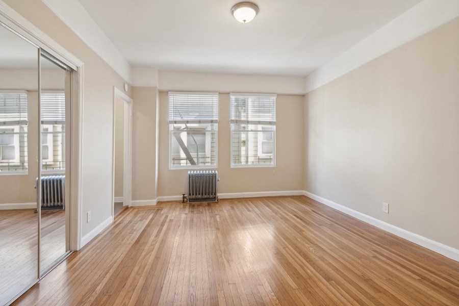 an empty living room with wood flooring and a mirrored closet
